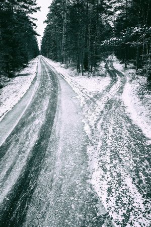 Asphalt road covered with snow leading through the forest. Winter scenery shown in black and white. Winter season.の写真素材