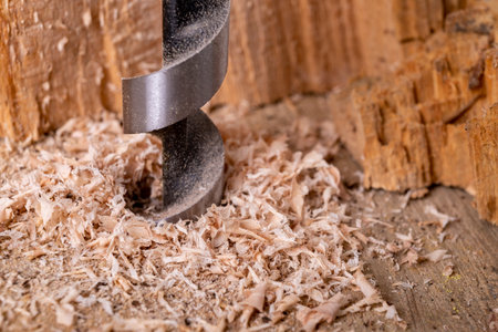 Drilling a hole in raw wood with a drill. Carpentry accessories in the workshop. Light background.の写真素材