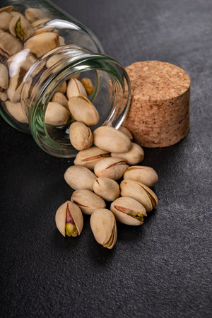 Pistachio nuts on a dark table. Salty snack in a jar. Dark background.の写真素材