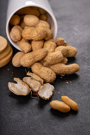 Peanuts on a dark table. Salty snack in a white ceramic container. Dark background.の写真素材