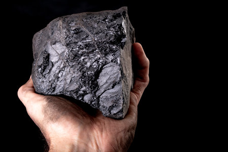 A lump of brown coal held on a dirty male hand. Material used for heating single-family houses. Dark background.の写真素材