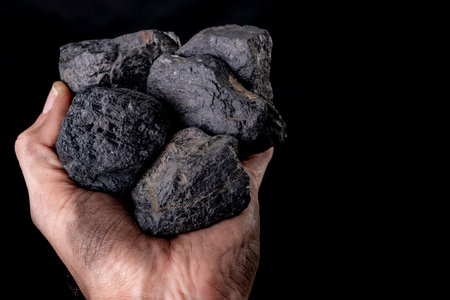 Chunks of brown coal held on a dirty male hand. Material used for heating single-family houses. Dark...