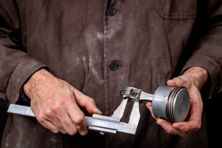 A mechanic measuring the piston of an internal combustion engine. Work in a mechanical workshop. Dark background.の写真素材