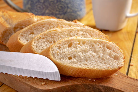 Tasty and fresh baguette cut into pieces. Bread and a chopping knife in the home kitchen. Light background.の写真素材