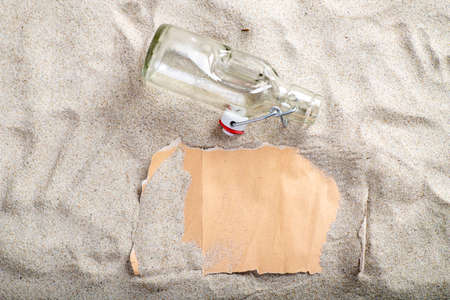 Gray blank paper covered with sand and a glass open bottle in the sand. The letter is on the beach. Summer season.の写真素材