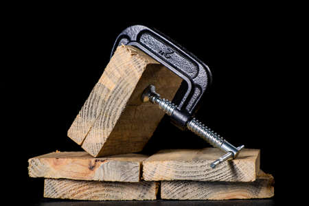 A metal clamp used to hold pieces of wood in place. Carpentry accessories in the workshop. Dark background.の写真素材