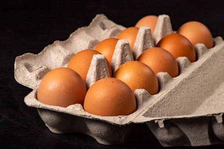 Fresh chicken eggs in a paper container. Dairy products prepared for serving. Dark background.