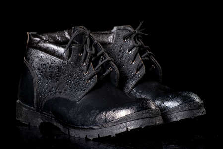 Black wet work boots on a dark table. Protective accessories for construction workers. Dark background.の写真素材