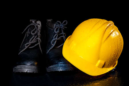 Black wet work boots and helmet on a dark table. Protective accessories for construction workers. Dark background.の写真素材