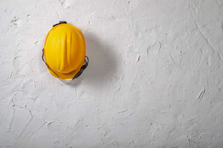 Yellow work helmet hung on a hook. Health and safety accessories on a white wall background. Light background.の写真素材