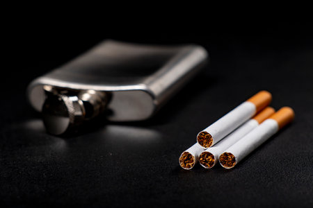 Metal flask and cigarettes. Metal container for alcohol and smoking tobacco. Dark background.の写真素材
