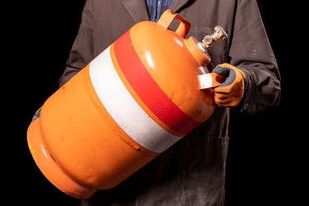 A production worker with a gas cylinder. Man carrying dangerous explosives. Dark background.の写真素材