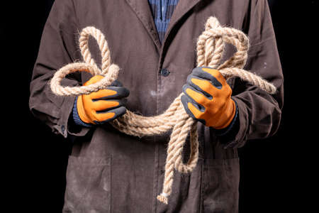 A production worker holding a thick rope in his hands. Construction worker working on the construction site. Dark background.の写真素材