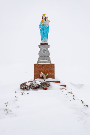 Lichnowy, Pomeranian Voivodeship Poland - February, 17, 2021: A statue of the Virgin Mary standing by the road. Catholic monument covered in snow. Winter season.のeditorial素材