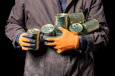 A production worker with canned meat. A man with a food ration with a long shelf life. Dark background.の写真素材