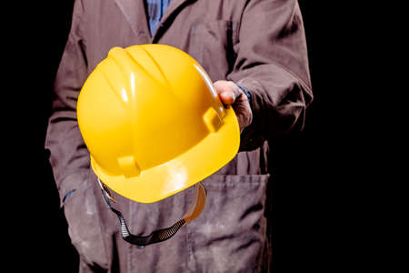 A production worker holding a yellow hard hat. Protective clothing in the workplace. Dark background.の写真素材