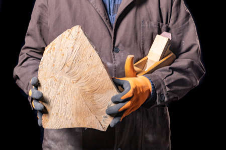 A carpenter with a piece of wood in his hands. A production worker in a workshop. Dark background.の写真素材