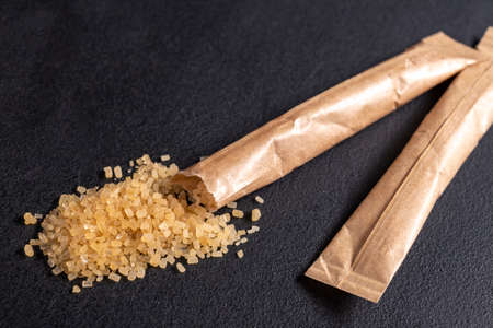 Spilled cane sugar from a small sachet. Preparation for sweetening beverages in a small package. Dark background.の写真素材