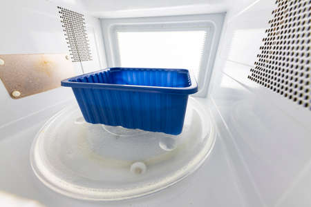 Plastic food container in a microwave oven. Preparing meals in the household. Light background.