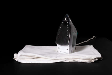 Iron for ironing on white linen. Accessories for small household chores. Dark background.