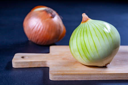 Onions put on a wooden board. Vegetables in the kitchen prepared for cutting. Dark background.の写真素材