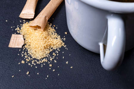 Spilled cane sugar from a paper bag. Sweetening tea with sugar. Dark background.の写真素材