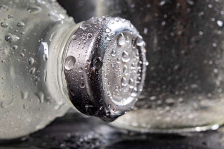 Glass bottles with fresh drinking water. Water drops on glass containers for water storage. Dark background.の写真素材