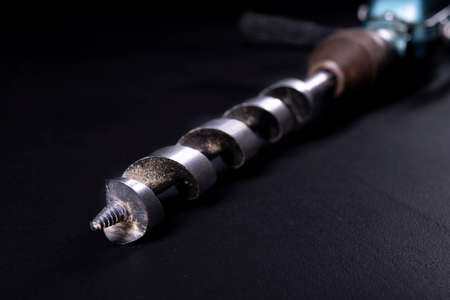 An old hand drill with a large drill bit. Tools for working in a carpentry workshop. Dark background.の写真素材