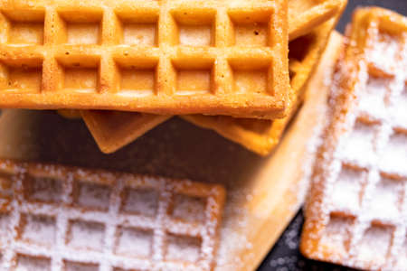 Sweet waffles prepared for serving. A tasty dessert eaten with fruit and preserves. Dark background.