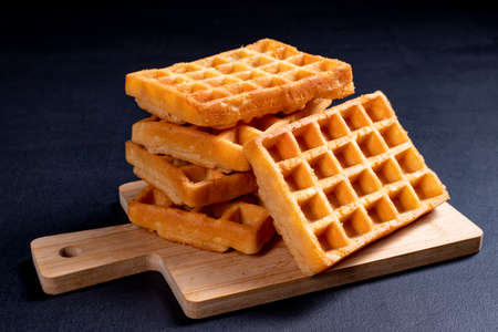 Sweet waffles prepared for serving. A tasty dessert eaten with fruit and preserves. Dark background.