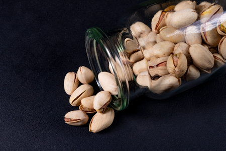 Pistachio nuts in a glass container. Salty snack on the kitchen table. Dark background.の写真素材