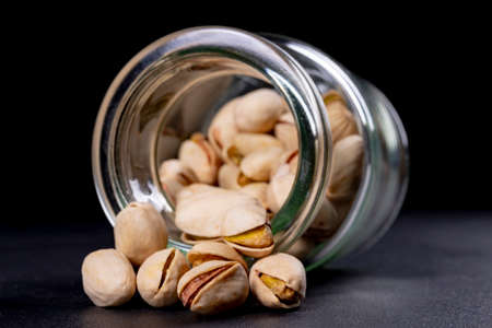 Pistachio nuts in a glass container. Salty snack on the kitchen table. Dark background.の写真素材