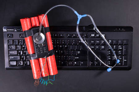 Medical stethoscope and dynamite on a computer keyboard. Diagnostics and repair of personal computers. Dark background.の写真素材