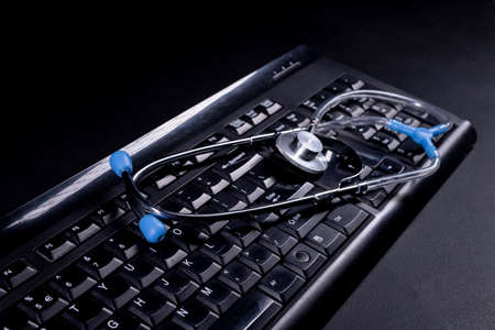 PC keyboard and medical stethoscope. Diagnostics and repair of personal computers. Dark background.の写真素材