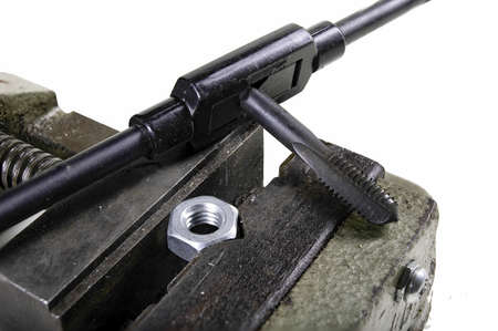 The screw nut in a vice while cutting a mechanical thread. Minor locksmith work in the workshop. Isolated background.の写真素材