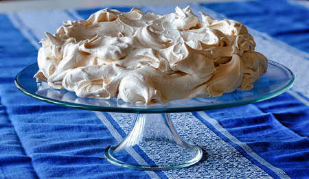 Meringue cake on a glass base placed on a table covered with a tablecloth.の写真素材