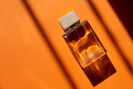 A bottle of perfume on an orange background with natural light and geometric diagonal shadows....