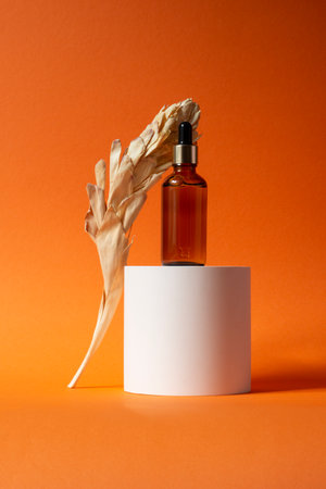 Amber glass dropper bottle with metallic lid on a piece of stone. Orange background with daylight. Skincare products , natural cosmetic. Beauty concept for face and body careの写真素材