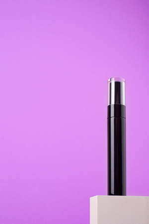 Black mascara tube with a transparent cover on a white podium and purple background. Makeup product for eyes with space for text.の写真素材
