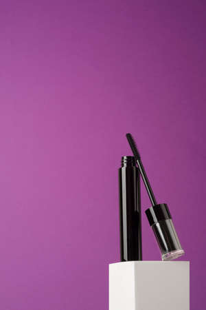 Open black mascara tube with a transparent cover and brush on a white podium and purple background. Makeup product for eyes with space for text.の写真素材