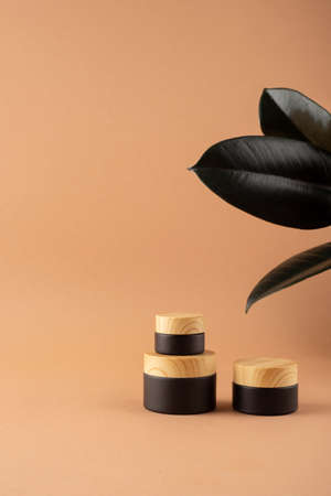 Black frosted glass jars with bamboo lid. Skincare concept on beige background with green dry plants. Natural cosmetic concept for face body careの写真素材