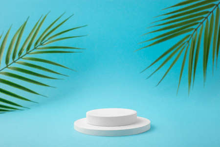 White podium for product presentation with tropical leaves on blue background. Skincare products ,...