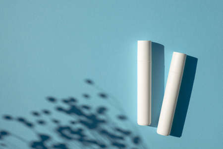 Two plastic white tubes for cream or lotion. Top view on blue background with plant shadow. Skincare cosmetic. Beauty concept for face body careの写真素材