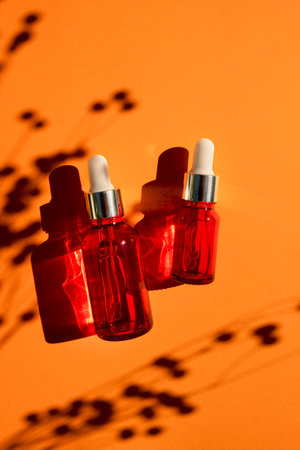 Red glass dropper bottle with silver lid on an orange background. Skincare products with beautiful daylight. Trending concept natural cosmetic with plant shadow.Beauty concept for face and body careの写真素材