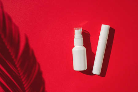 Plastic white roller tube and bottles with pump for cream or lotion. Top view on red background with...