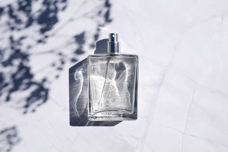 Transparent bottle of perfume with spray on white marble surface. Clear glass without lid. Trending concept in natural materials with plant shadow. Luxury presentation.の写真素材