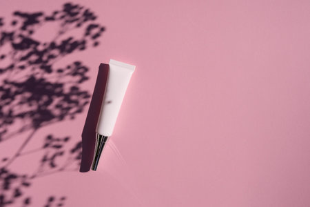 Plastic white tube eye cream with metal lid and narrow tip. Top view on lilac background with plant shadow. Skincare cosmetic. Beauty concept for face body careの写真素材