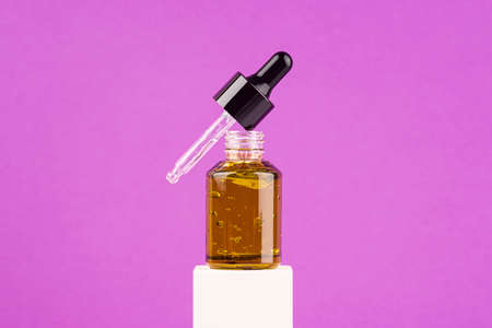 Open green glass dropper bottle with pipette on the white podium on purple background. Gel texture with bubbles in a container. Skincare products , natural cosmetic. Beauty concept for face and body care.の写真素材