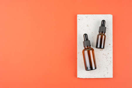 Amber glass dropper bottles different sizes with black lid on stone plate. Trending concept in natural materials on terracotta color background. Presentation backdrop for text or advertising.の写真素材