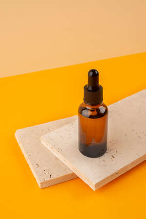 Amber glass dropper bottle with black lid on stone plate. Trending concept in natural materials on orange color background. Presentation backdrop for text or advertising.の写真素材